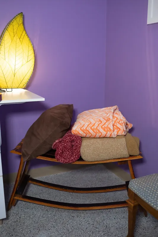 Quiet corner of the clinic with a wooden rocking bench, soft blankets and a warm leaf-shaped lamp