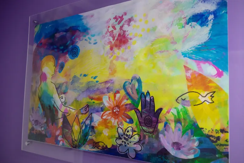 Colourful abstract painting of flowers, hands and a heart displayed on the clinic wall