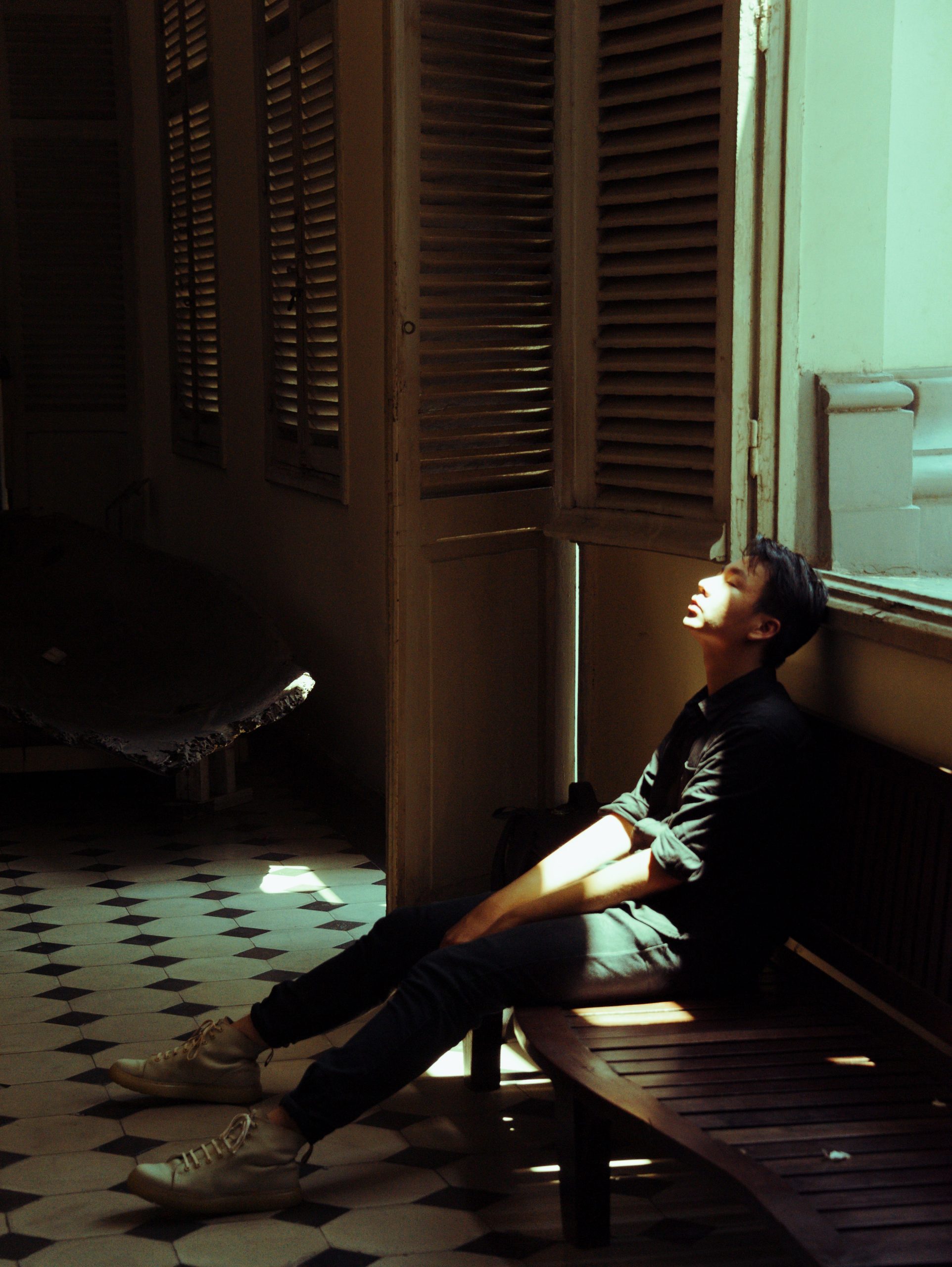 a young man sits on a bench in a dark room, with light slanting across his face.