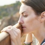 a woman stands with her face pressed up to a fence, looking depressed